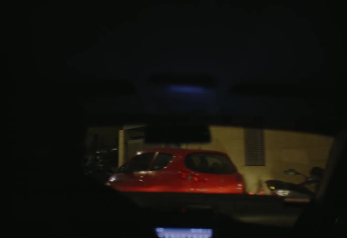 A person is driving down the street at night with cars parked along the side of the road