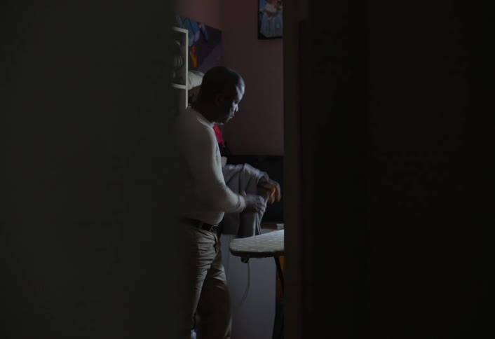 A man opens the ironing board and plugs in an iron