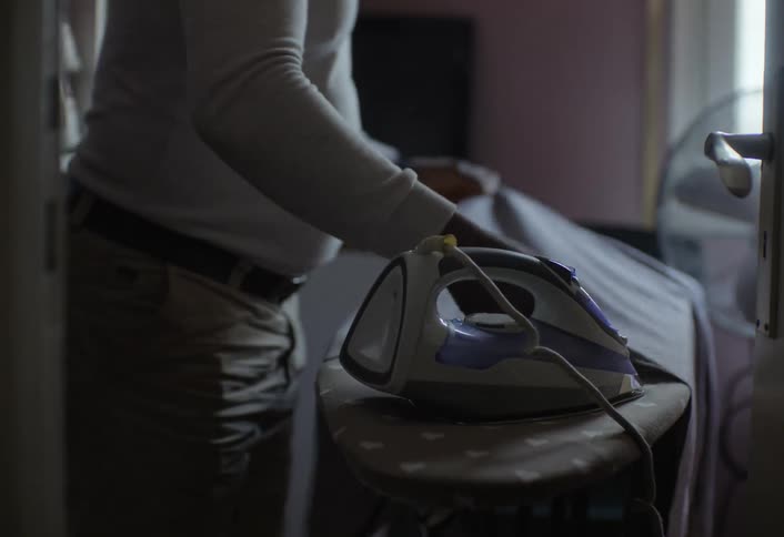 A man is ironing his clothes indoors at midday
