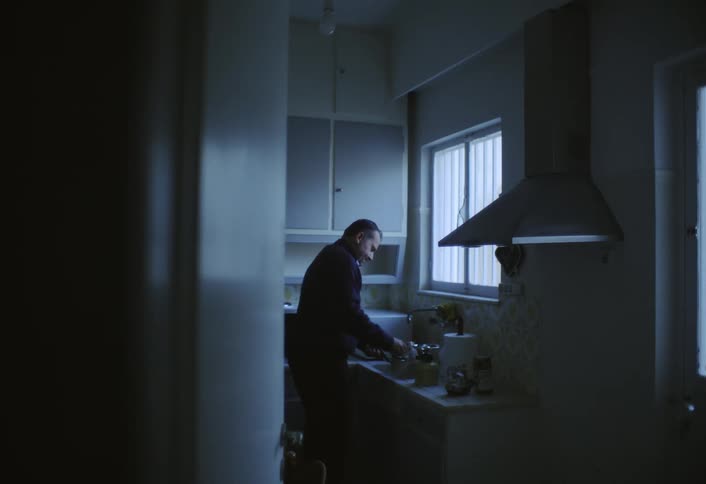 A man prepares coffee alone in a dimly lit kitchen
