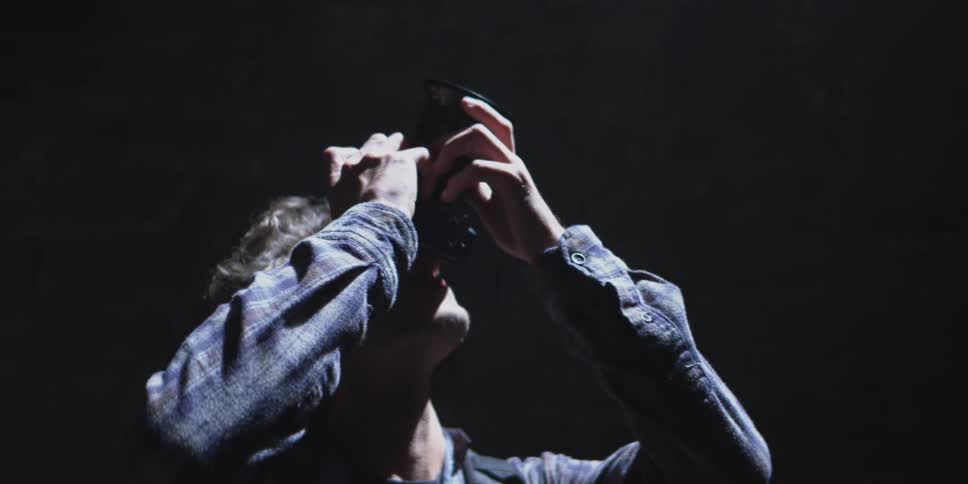A man looks upward through a camera illuminated dramatically in a dark environment