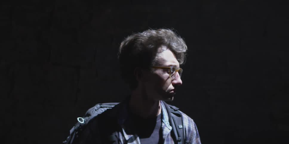 A man with a backpack walks through a dark area with dramatic lighting