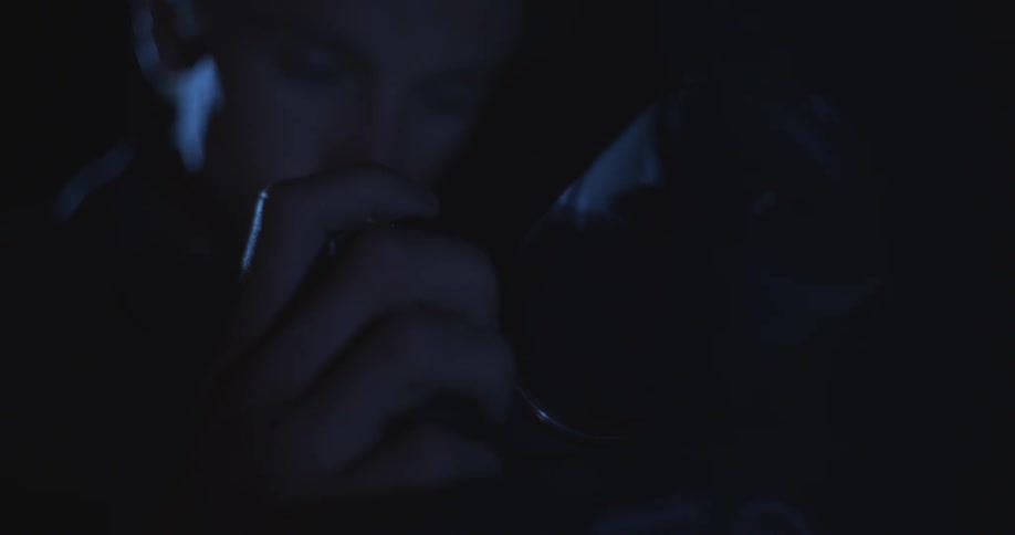 A person closely examines or adjusts something in dim light their face partially obscured in the shadows