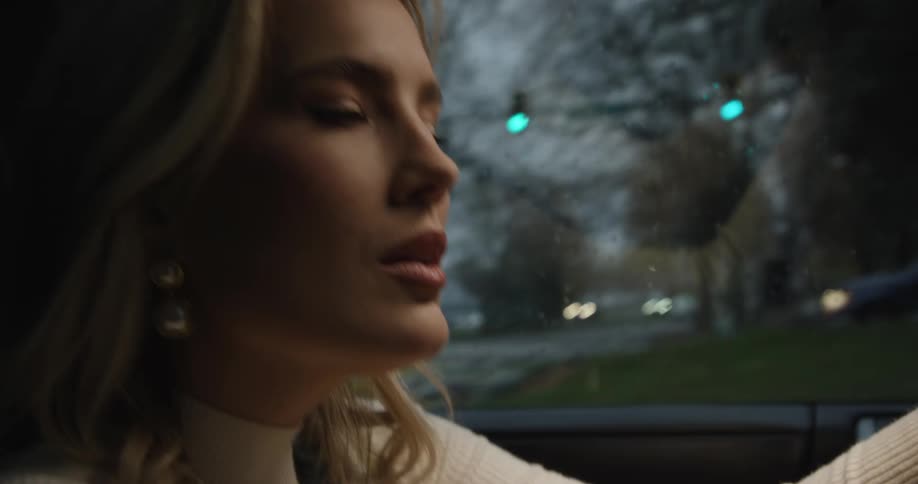 A woman in a cream sweater looks ahead with focus while driving at dusk