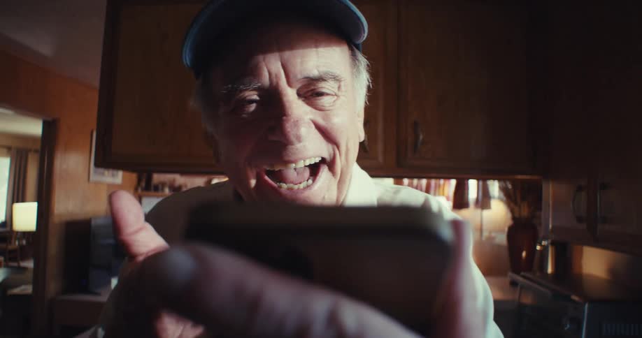 Elderly man waves and smiles during a video call while standing in his home