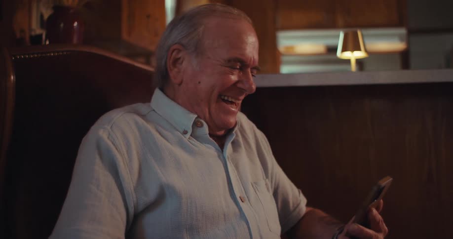 Elderly man sitting laughing and holding a smartphone