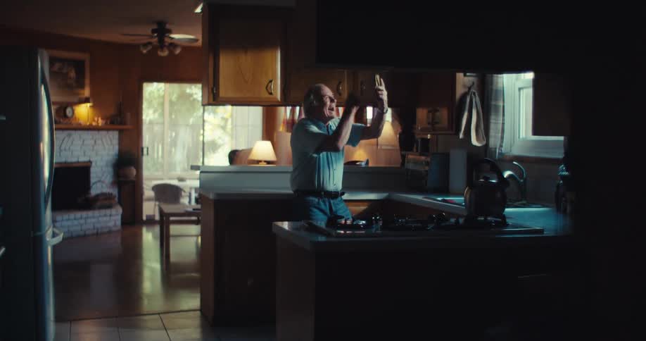 Elderly man viewing his smartphone while standing in his kitchen cheers in excitement