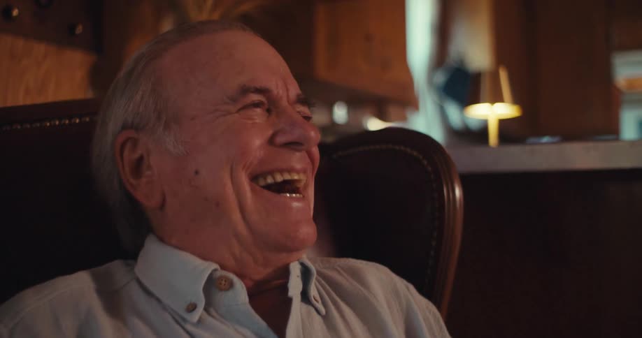 Old man laughs heartily while looking at his phone