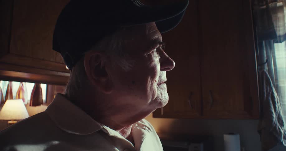 Elderly man standing in his kitchen during the daytime smiles before looking out the window