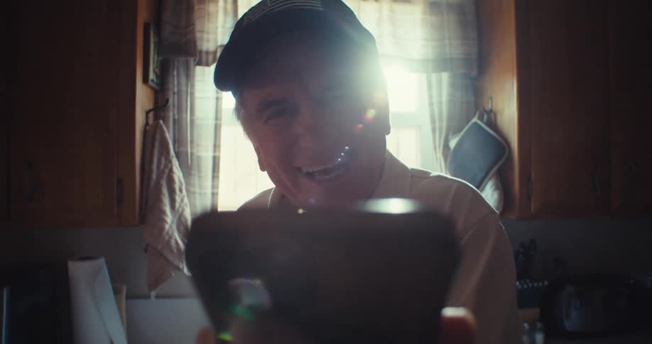 A man smiles warmly during a video call in a sunlit kitchen