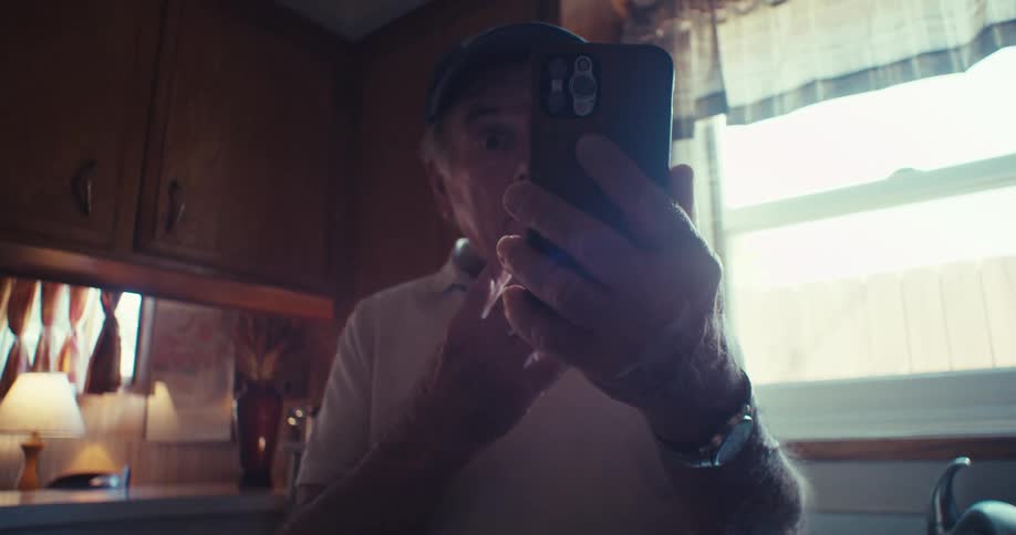 Elderly man holding cell phone facetiming in his kitchen