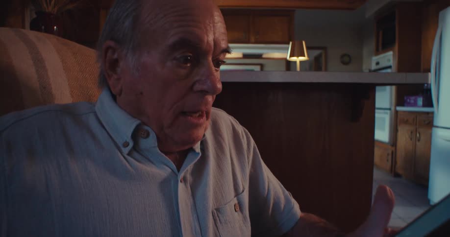Elderly man sitting at home using his smartphone is surprised and pleased by what he sees on it