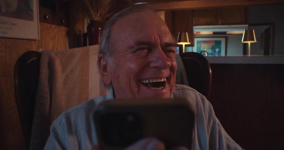 Happy elderly man laughing while interacting with a smartphone