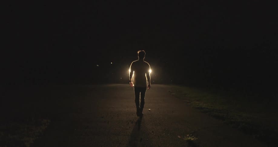 Man approaches a vehicle with shining headlights at night