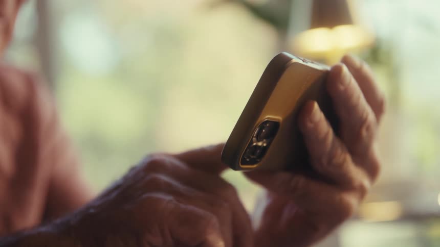 An elderly person uses a smartphone closely focused on their hands and the device