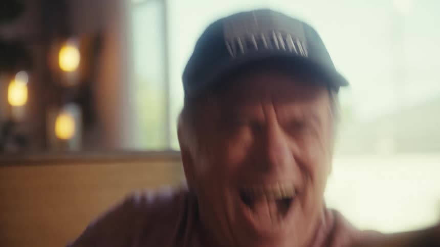 An elderly man watching a game on his mobile device becoming super excited as he bounces up and down in his chair raising his hand and laughing at midday