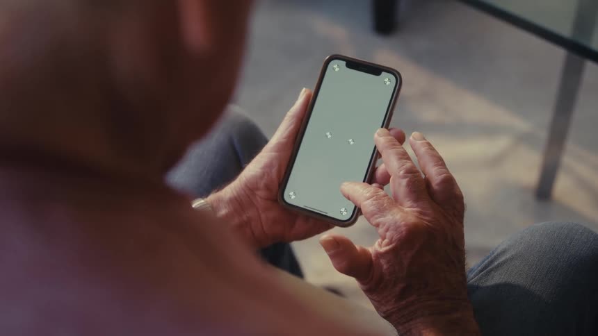 Elderly man scrolls on his smartphone while sitting down