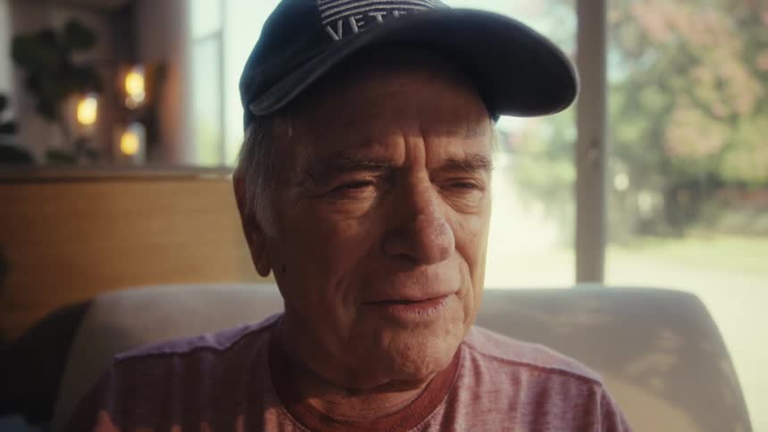 Elderly man smiles and talks while sitting in his living room during daytime