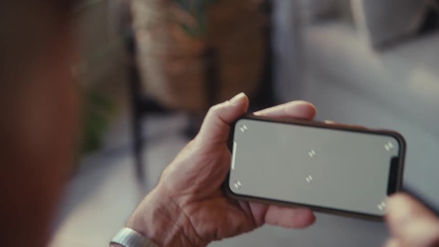 Elderly man vibrating while holding and watching on a smartphone