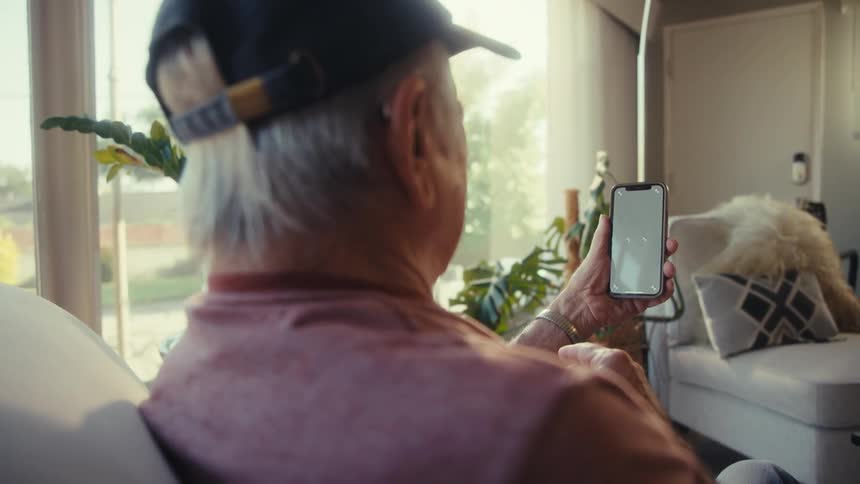 Elderly man sitting holding a smartphone in front of his face