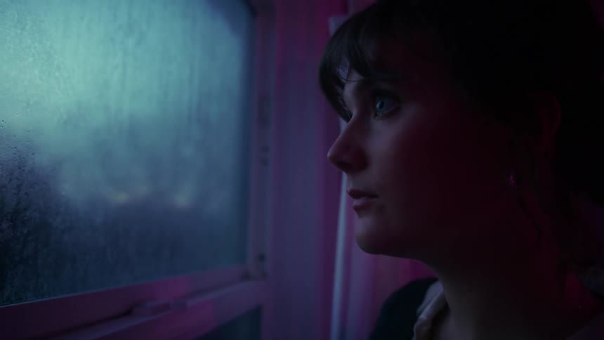 A young woman standing beside a glass window looking sad