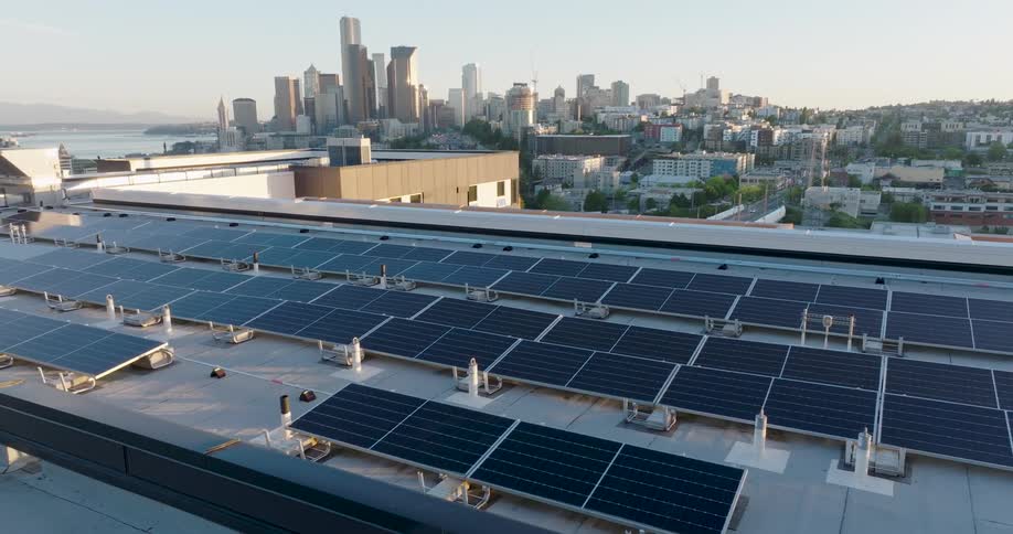 Dappled light filters onto solar panels that line the roof of a new apartment building with a city skyline in the distance
