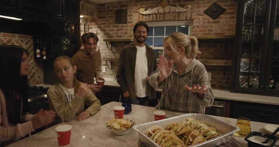 Woman placing a plate on a table and family members around her watch