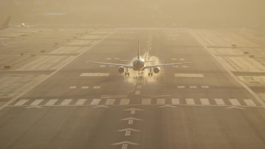 The video shows a plane on a runway viewed from behind with bright sunlight reflecting off the wet surface the runway has clear markings and the plane appears to be preparing for takeoff or has just landed