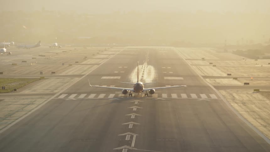 A commercial airplane is captured mid take off on a long wide airport runway on a hazy day