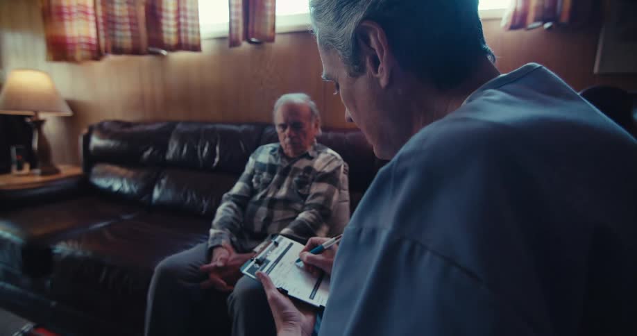 Close up of a male medical personnel taking history of an elderly male patient in a living room