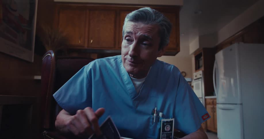 A person in blue scrubs sits in a home setting pointing at a brochure and explaining medical services