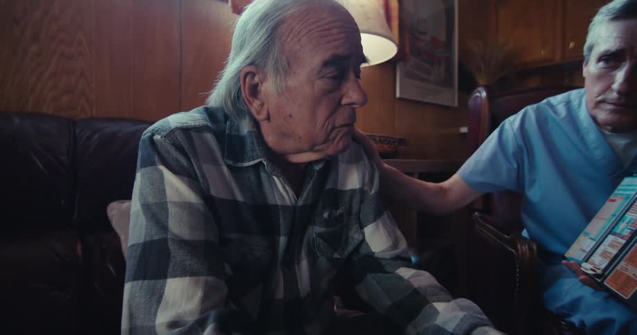 A caregiver attentively listens as the elderly man gestures during a conversation
