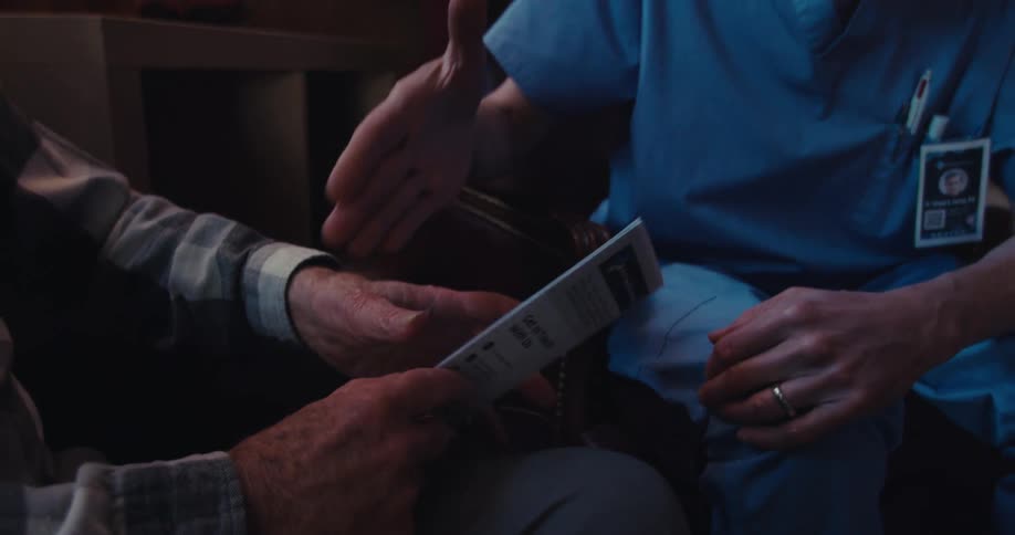An elderly man holds a healthcare brochure while speaking with a caregiver then the men shake hands