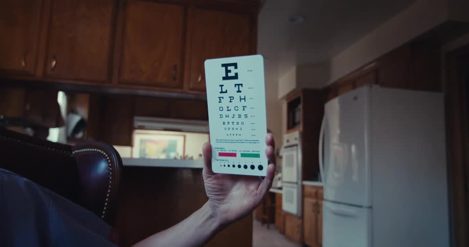 A caregiver holds up an eye chart in a kitchen setting for a vision test