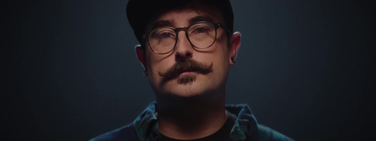 Man with a curly mustache raises his head and the light falls on his face