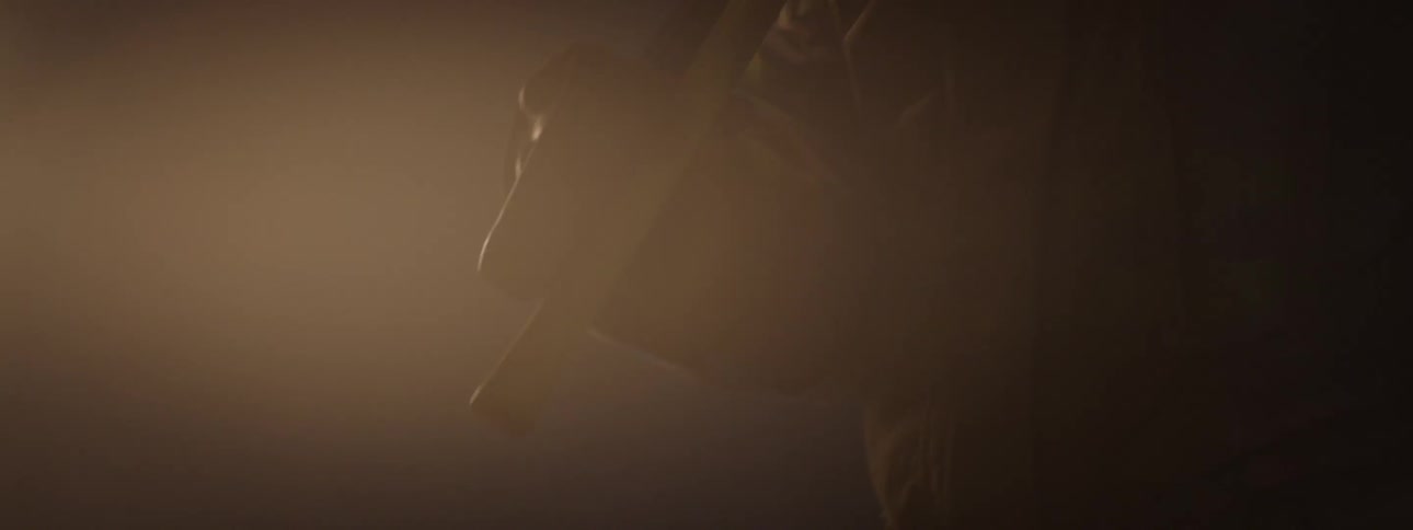 A black man stands looking sad holding a stick in a dark foggy room