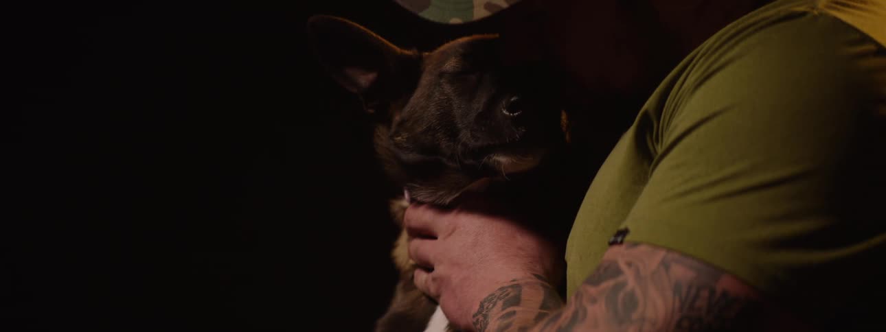 A man is holding a dog and kisses the dog under a black background
