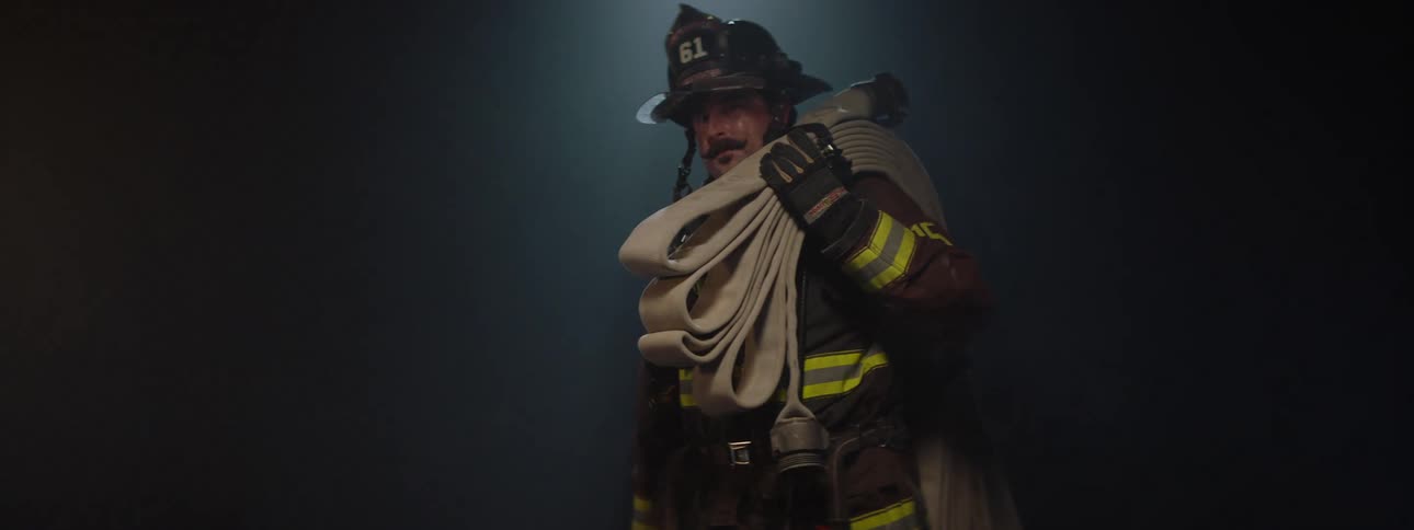 Fireman carrying a folded hose on his shoulder and a crowbar in his other hand