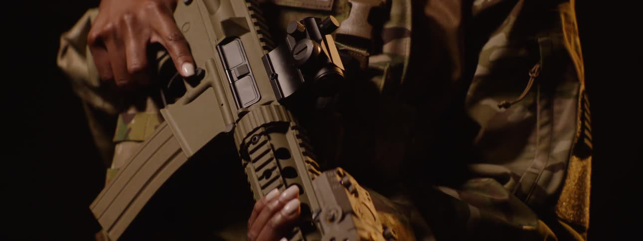 Close up of a female military personnel carrying a firearm while standing under yellow lighting
