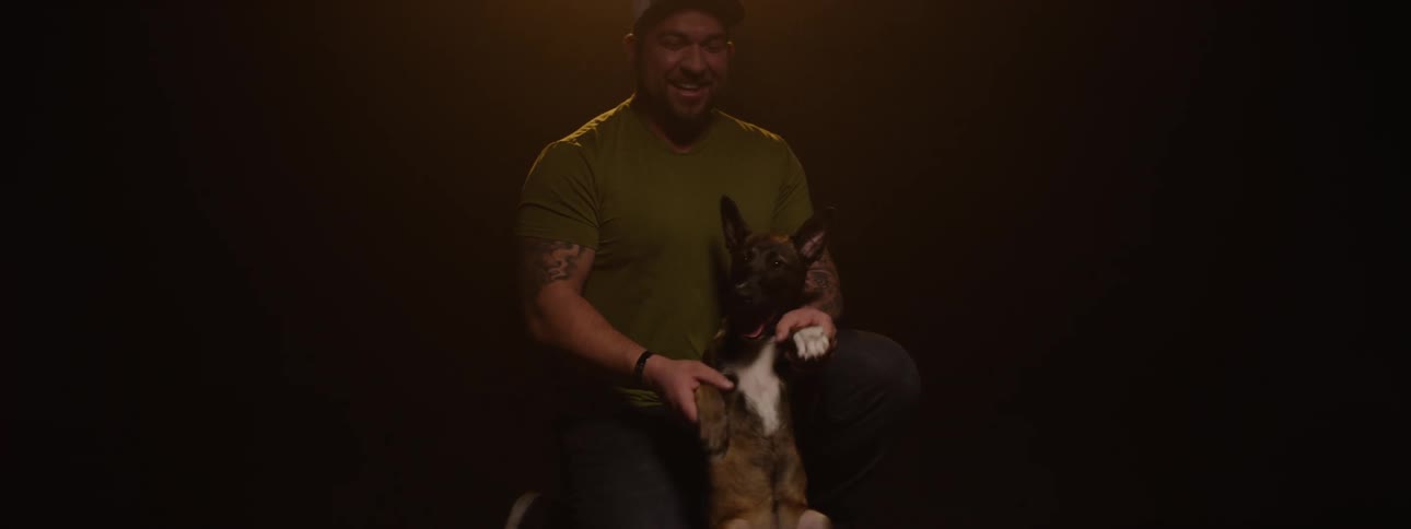 The man is petting his dog and holding its paws