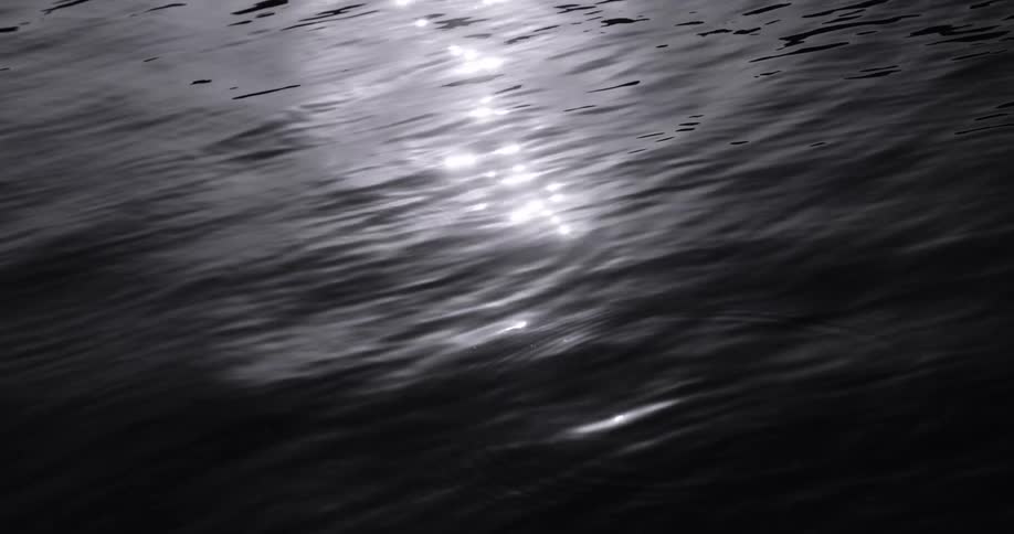 Ripples flow outward from multiple spots as waves move across the reflective surface of the water at night