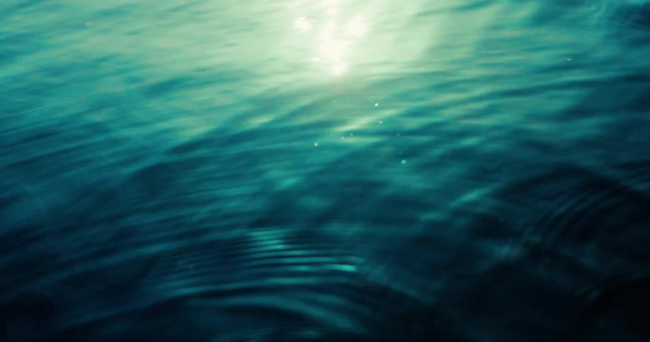 The video displays an abstract underwater scene with light rippling across the surface creating dynamic patterns and reflections the water is a deep bluegreen and small particles are visible floating in the illuminated areas