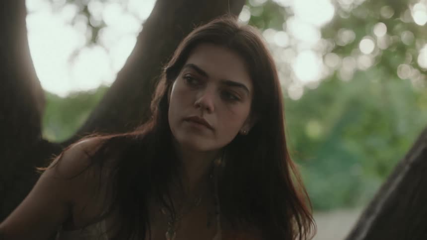 A young woman with long hair sitting beside a tree