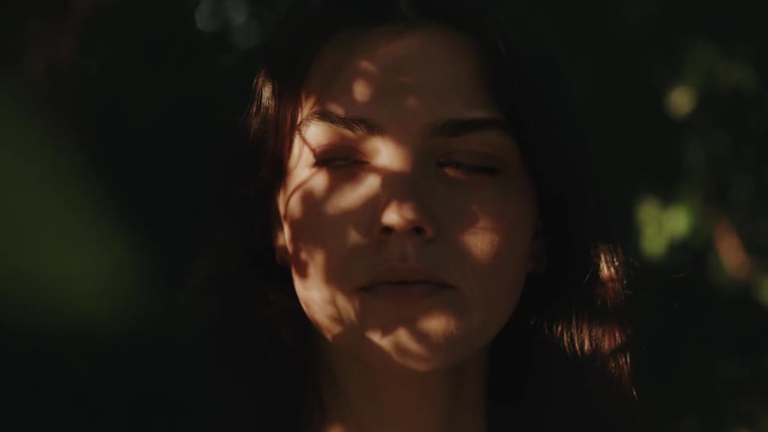 A young woman in nature in dappled sunlight