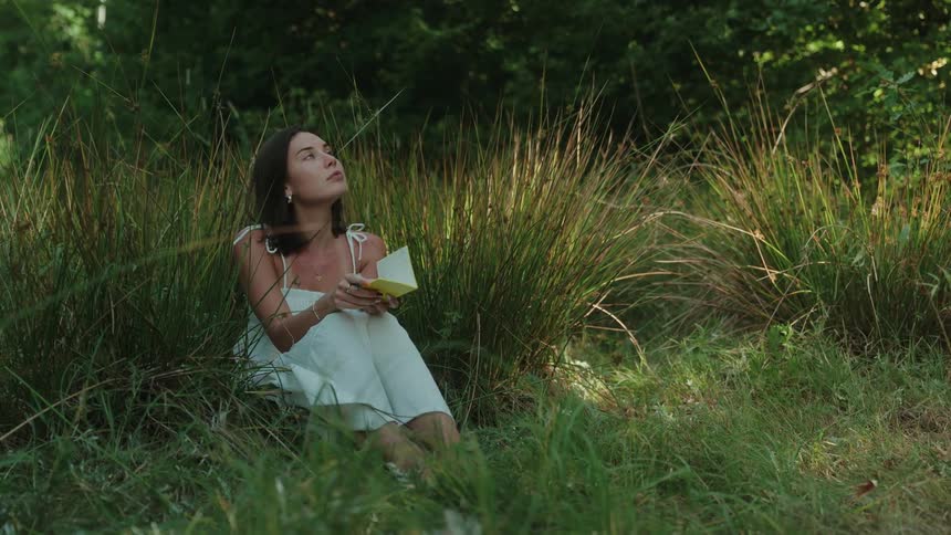 A young woman sitting on the grassland floor writing at midday