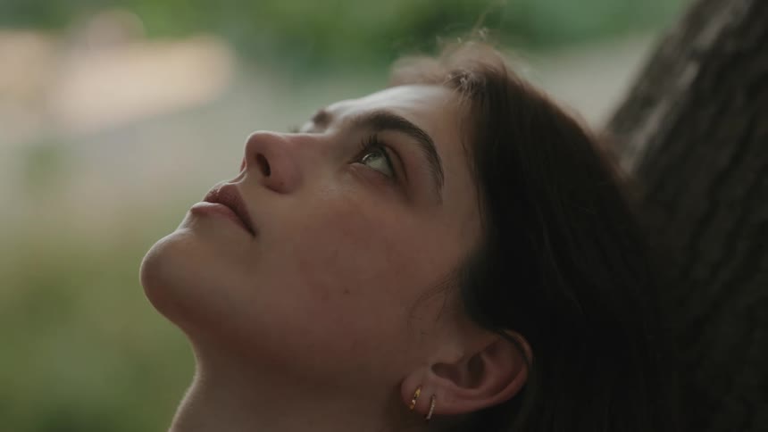 Woman moves a hand through her hair while leaning against a tree