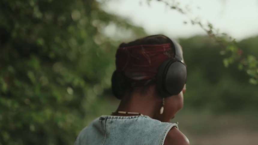 Woman wearing headphones with a happy expression in an outdoor setting with trees
