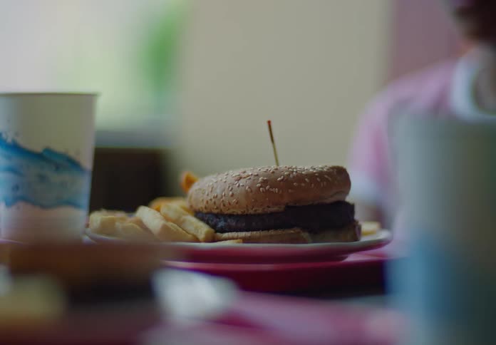 A burger and fries on a plate served in front of a teenage girl at a restaurant during midday
