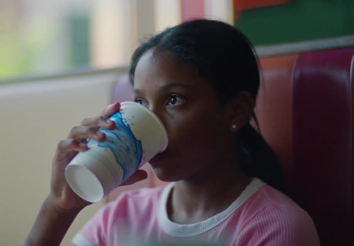 A girl drinks from a cup while sitting at a diner booth
