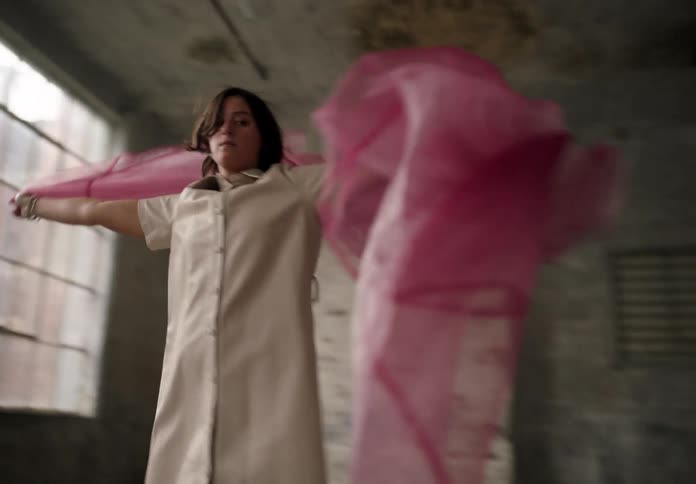 A woman twirls with a flowing pink scarf in a loft like room